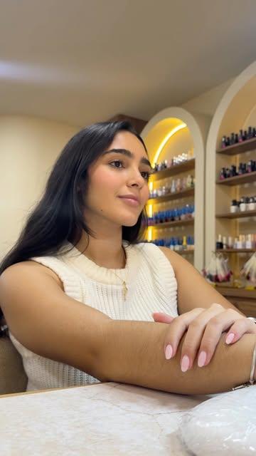 Clienta en una mesa de manicura frente a los nichos en arco con luz cálida